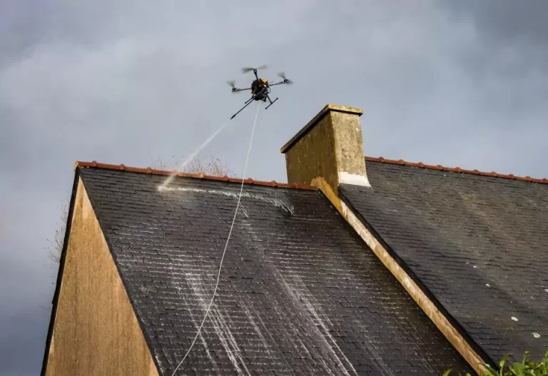 Un homme utilise un tuyau d'arrosage pour nettoyer un toit, projetant de l'eau pour enlever la saleté et les débris.